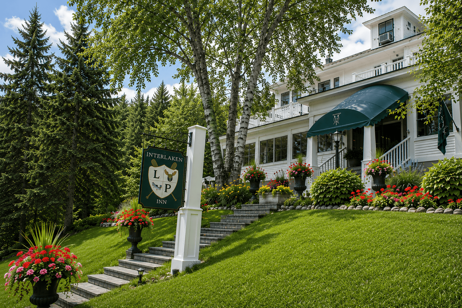 A charming inn with a sign surrounded by lush gardens and tall trees.