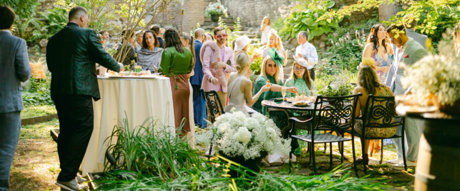 A lively outdoor gathering with guests enjoying food and conversation amidst lush greenery.