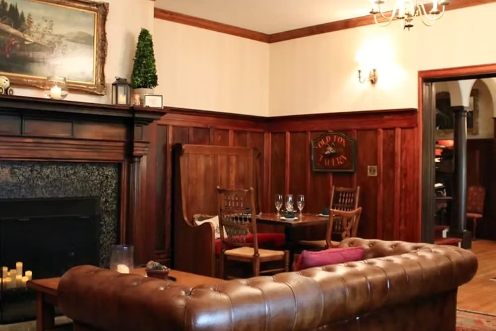 A cozy living room featuring dark wood paneling, a leather sofa, and a small dining table set.