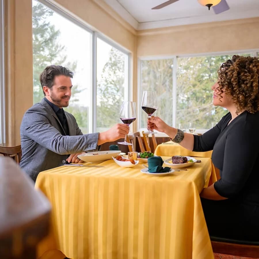 A man and woman toast with glasses of red wine at a beautifully set table in a cozy restaurant.