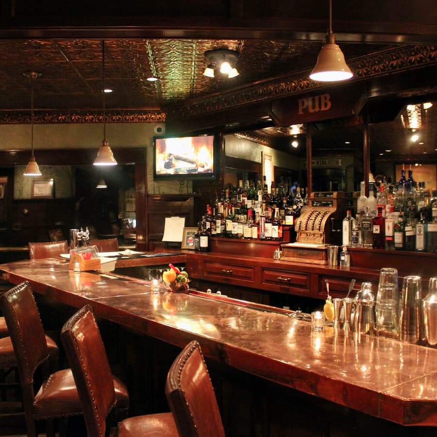 A dimly lit pub bar featuring a polished counter and a variety of liquor bottles behind it.